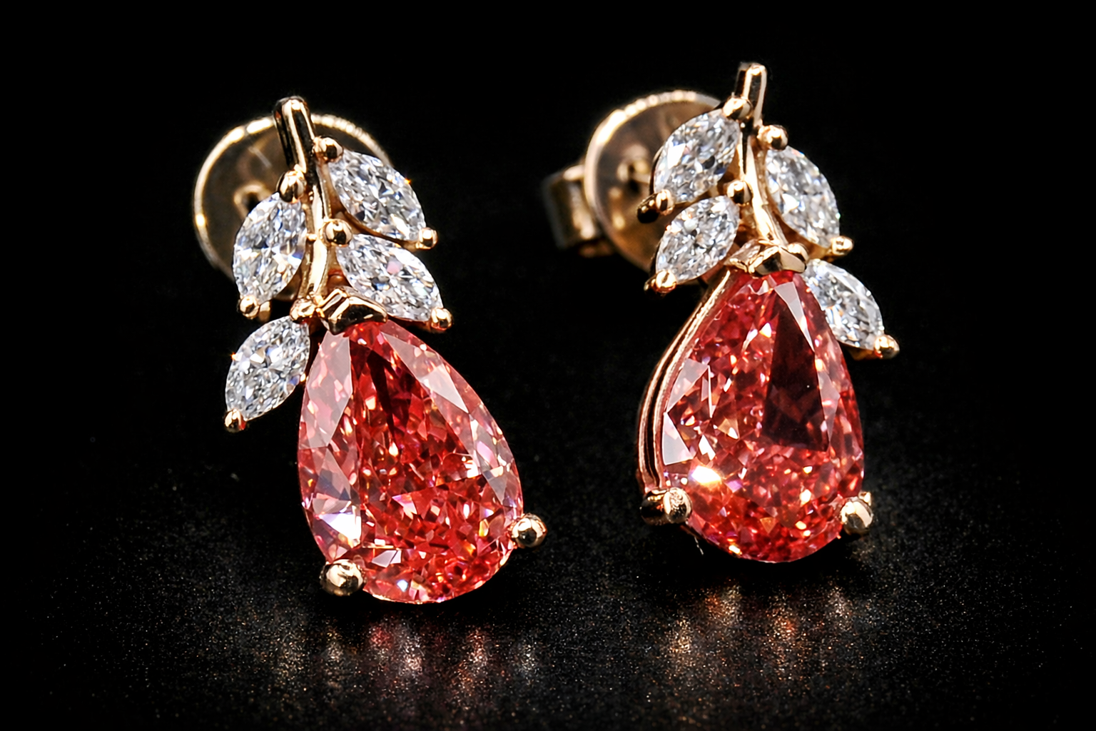 Pair of earrings with red teardrop-shaped gemstones and gold and diamond accents on a black background.